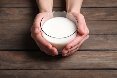 Photo of Woman holding glass of milk at wooden table, closeup