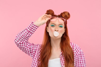 Beautiful woman with bright makeup blowing bubble gum on pink background