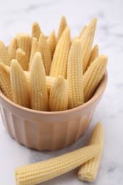 Photo of Bowl and pickled baby corn on white marble table, closeup