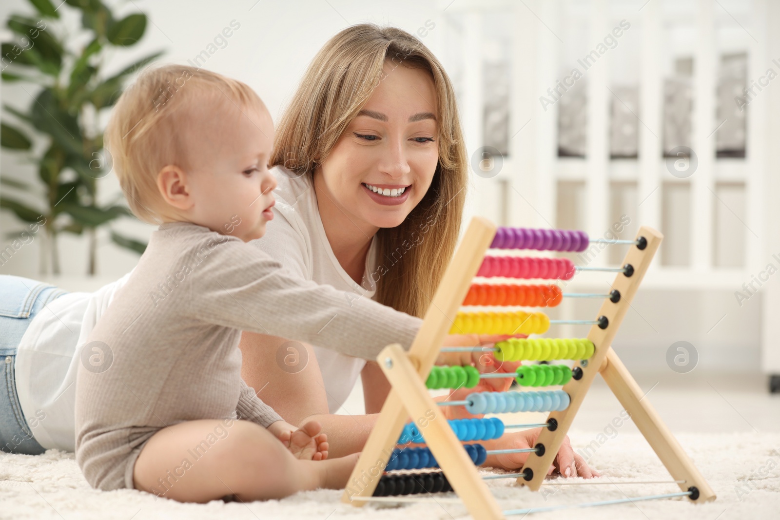 Photo of Children toys. Happy mother and her little son playing with wooden abacus on rug at home