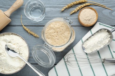 Leaven, flour, water, whisk and ears of wheat on grey wooden table, flat lay