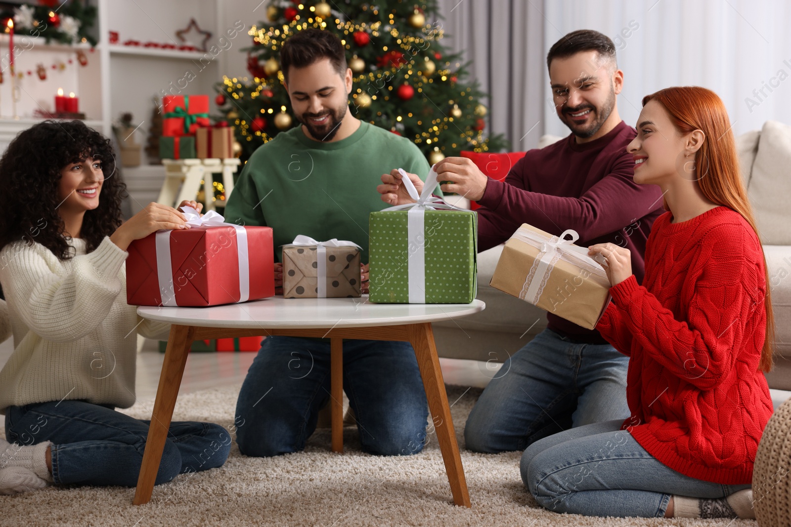 Photo of Christmas celebration in circle of friends. Women and men opening gifts at home