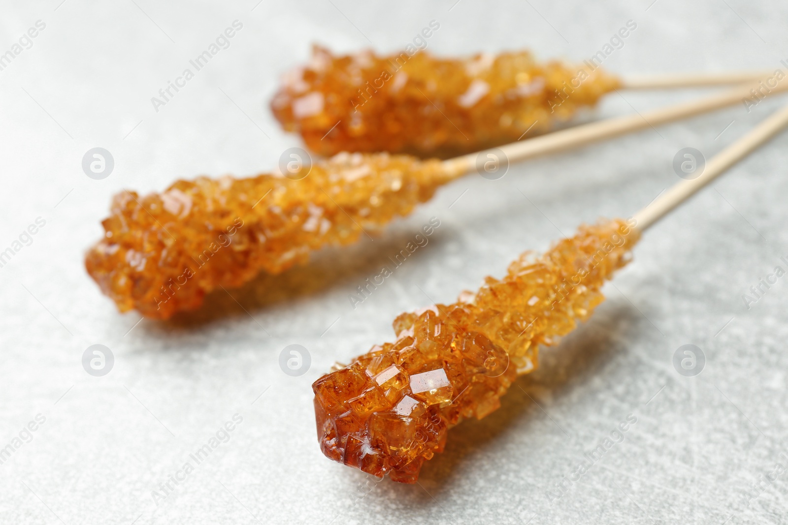 Photo of Sticks with sugar crystals on light grey table, closeup. Tasty rock candies