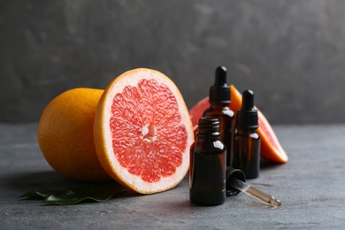 Photo of Bottles of essential oil and grapefruits on grey table