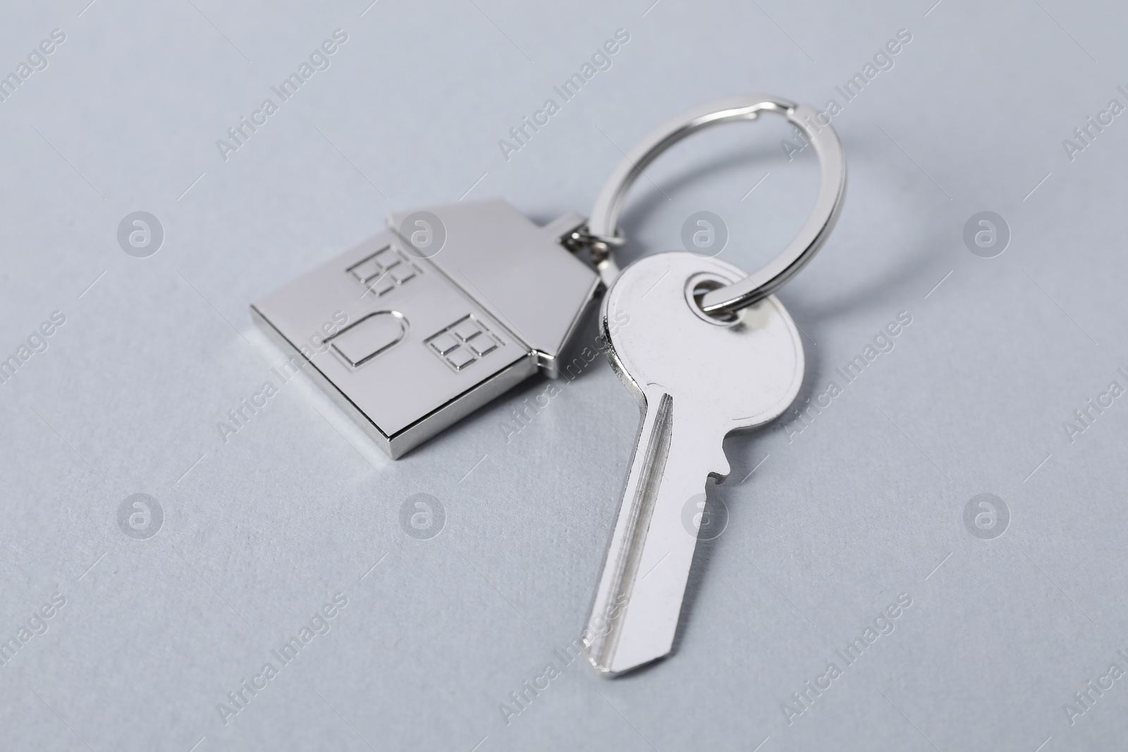 Photo of Key with keychain in shape of house on light grey background, closeup