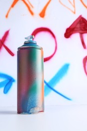 One spray paint can near white wall with different drawn symbols