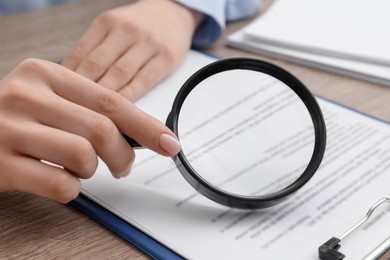 Woman looking at document through magnifier at wooden table, closeup. Searching concept