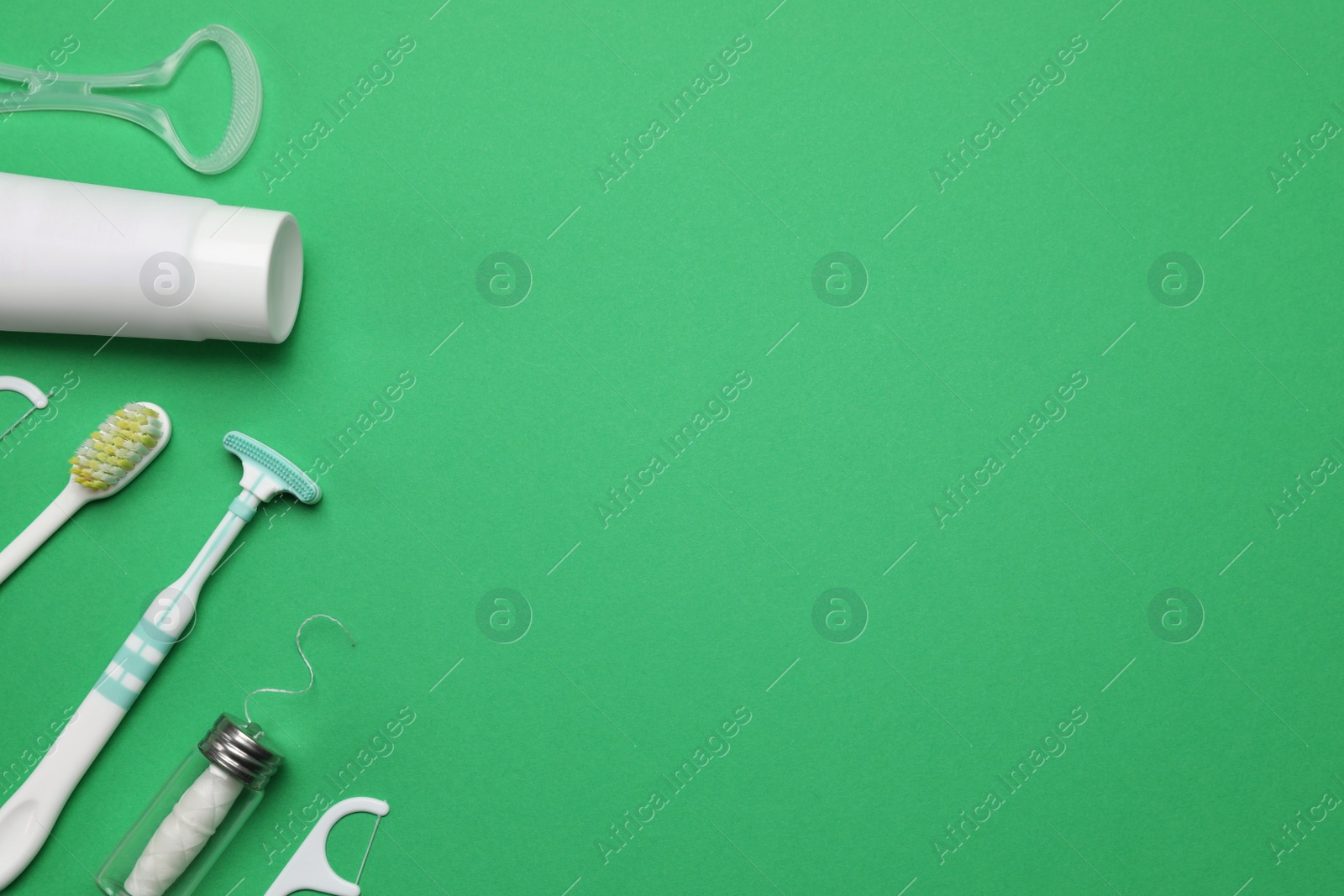 Photo of Flat lay composition with tongue cleaners and teeth care products on green background, space for text