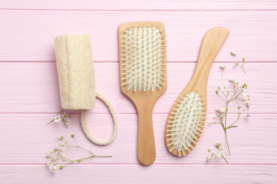 Hair brushes, bast wisp and small white flowers on pink wooden background, flat lay