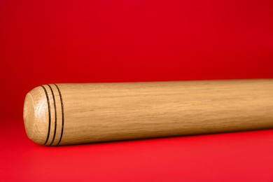 Photo of Wooden baseball bat on red background, closeup. Sports equipment