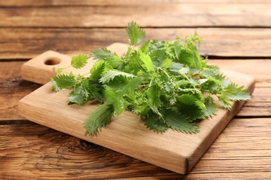 Photo of Board with fresh stinging nettle leaves on wooden table