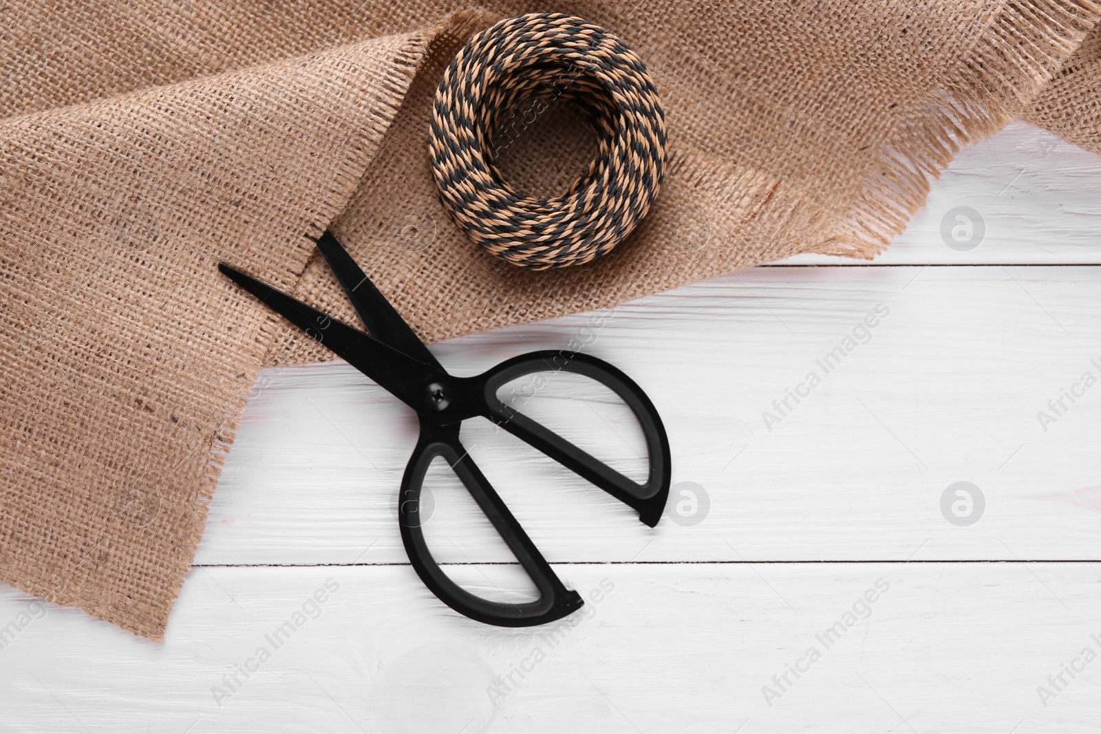 Photo of Burlap fabric, thread and scissors on white wooden table, flat lay. Space for text