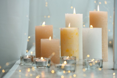 Beautiful burning candles and fairy lights on windowsill indoors