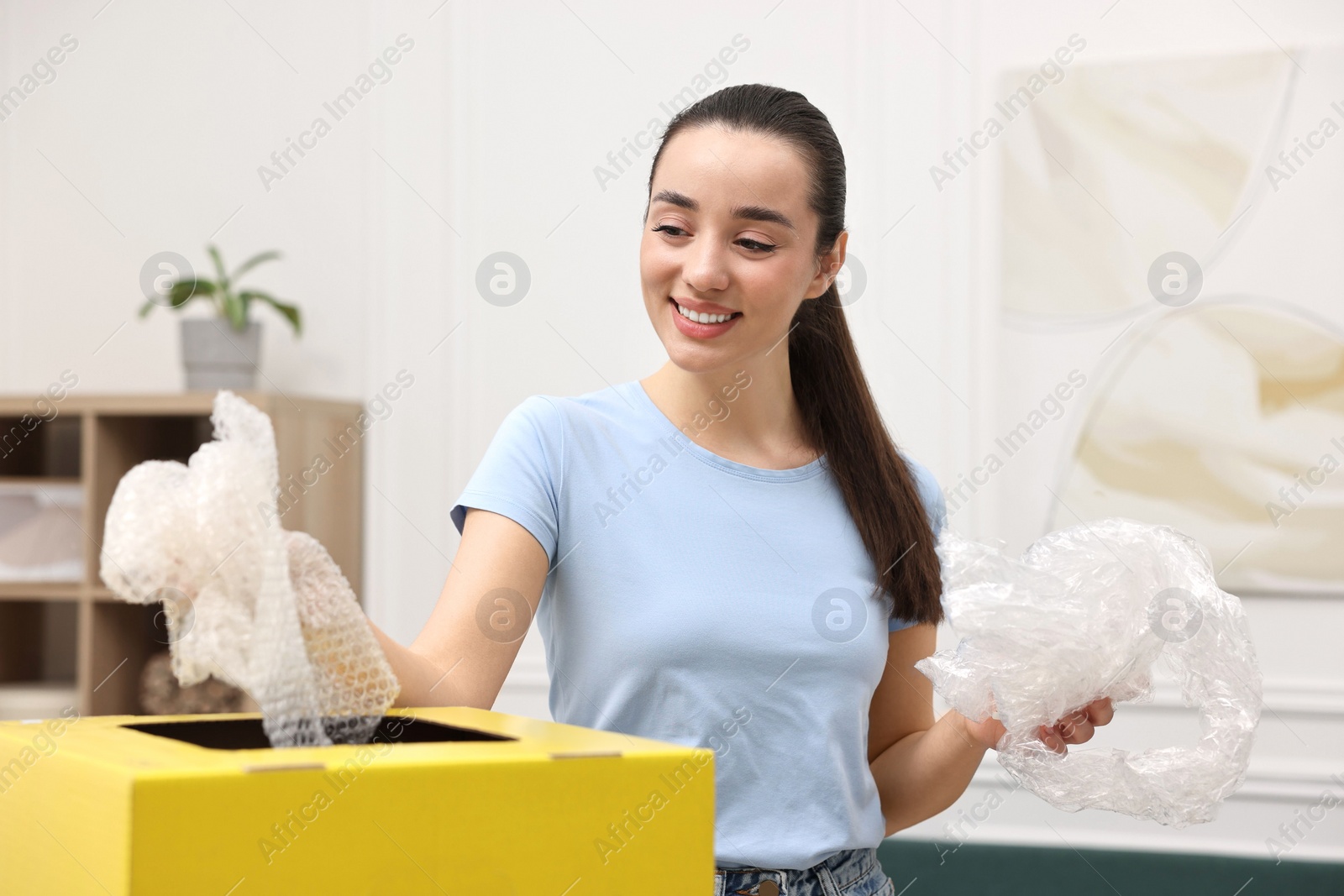 Photo of Garbage sorting. Smiling woman throwing plastic package into cardboard box in room