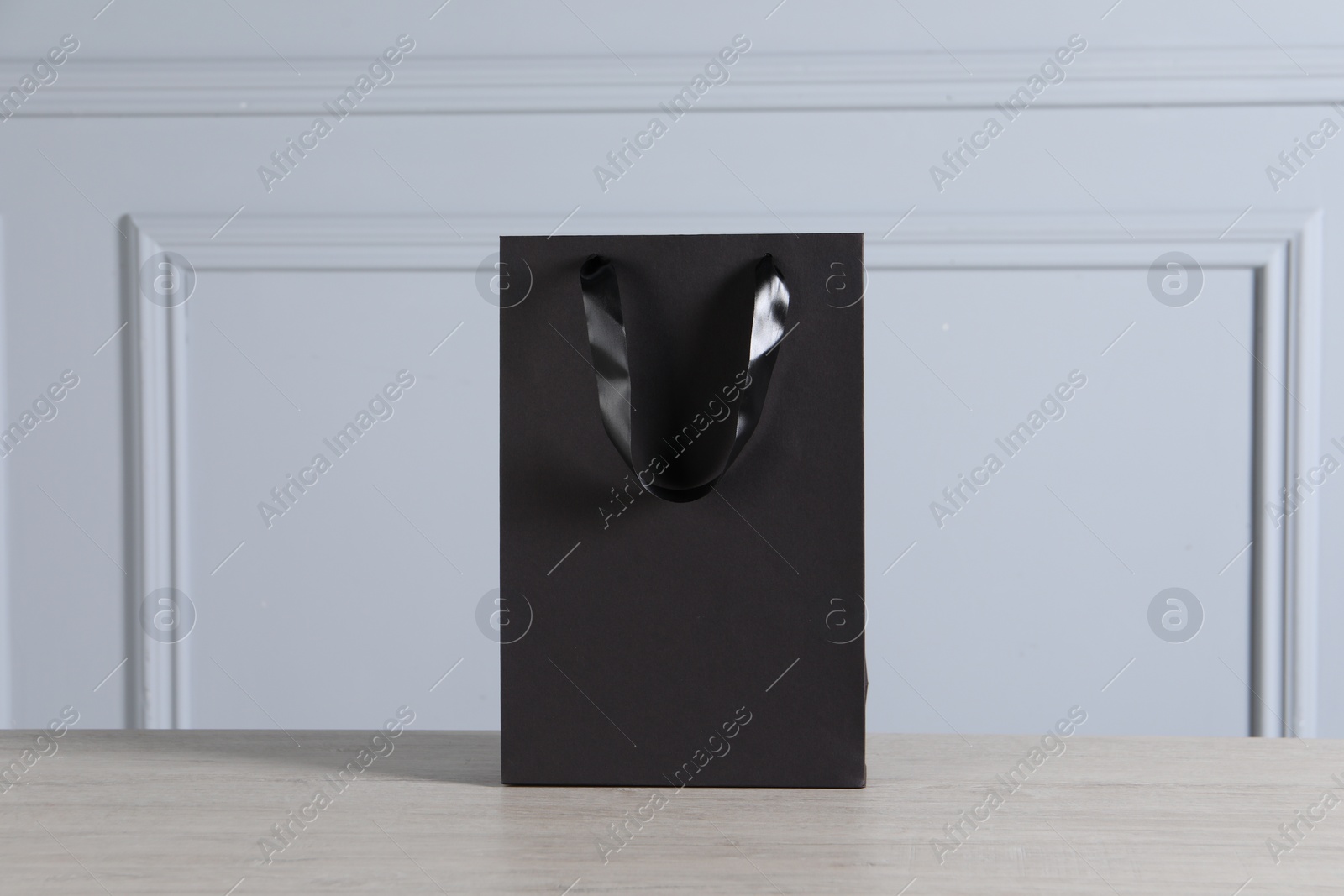 Photo of Black paper bag on wooden table against light grey wall