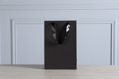 Black paper bag on wooden table against light grey wall