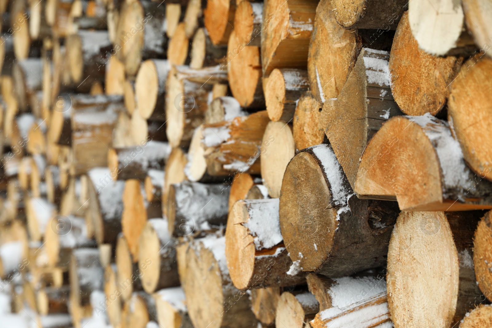 Photo of Stacked firewood with snow as background, closeup. Heating house in winter