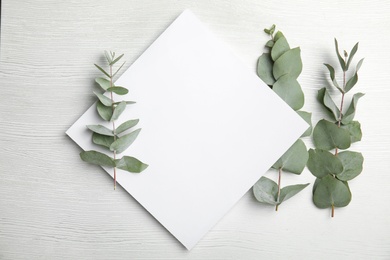 Photo of Fresh eucalyptus leaves and blank card with space for design on wooden background, top view