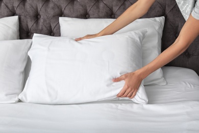 Photo of Young woman plumping white pillow on bed, closeup