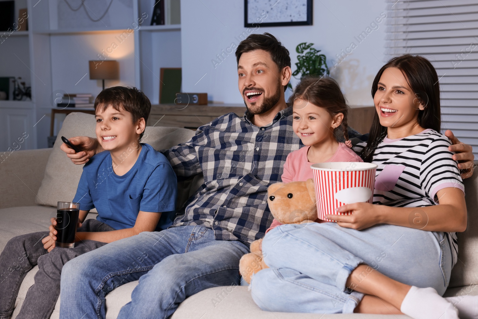 Photo of Happy family watching movie at home in evening. Father changing TV channels with remote control