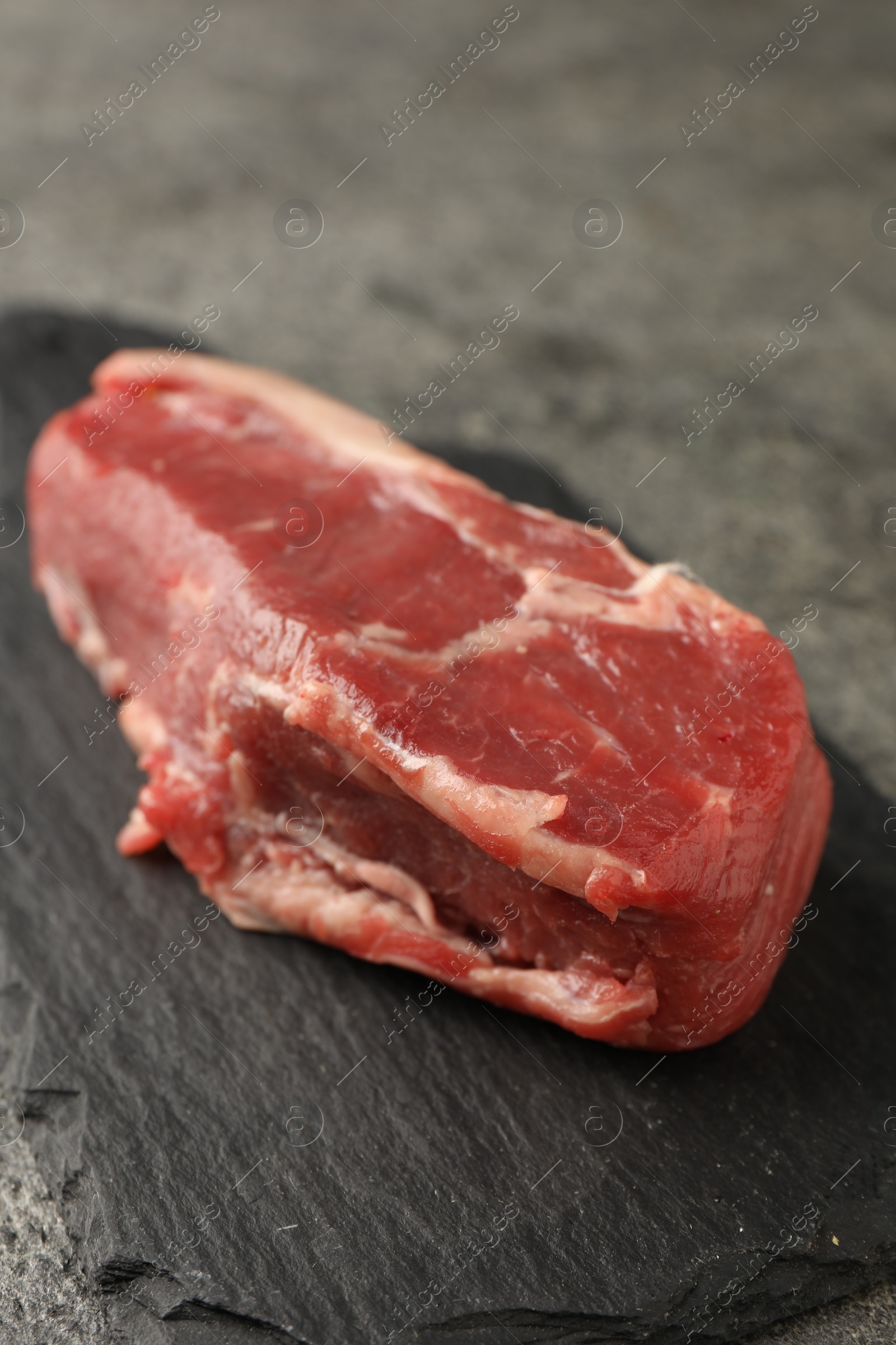 Photo of Piece of raw beef meat on grey table, closeup
