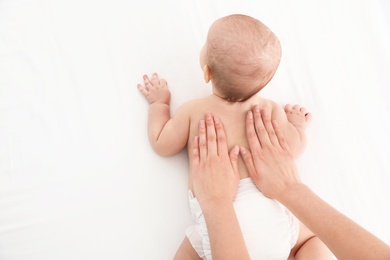 Top view of mother and her cute child on white bed, space for text. Baby massage and exercises