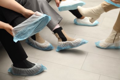 Women wearing blue shoe covers onto different footwear indoors, closeup