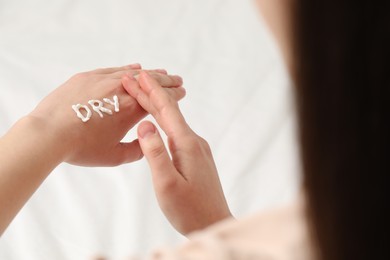 Young woman with word Dry made of cream on her hand on bed, closeup