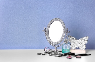 Photo of Stylish mirror, makeup products and accessories on table near light wall