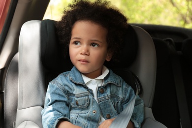 Photo of Cute African-American child sitting in safety seat inside car. Danger prevention