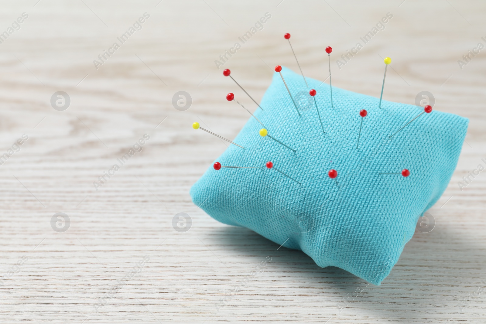 Photo of Light blue pincushion with sewing pins on wooden table. Space for text