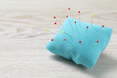 Light blue pincushion with sewing pins on wooden table. Space for text