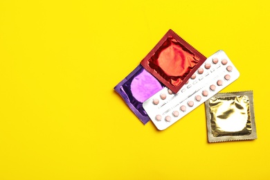 Condoms and birth control pills on yellow background, flat lay with space for text. Safe sex concept