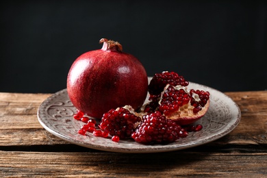 Photo of Plate with ripe pomegranates on table against black background