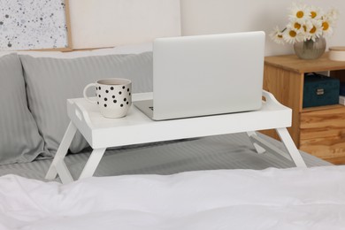 Photo of White tray table with laptop and cup of drink on bed indoors