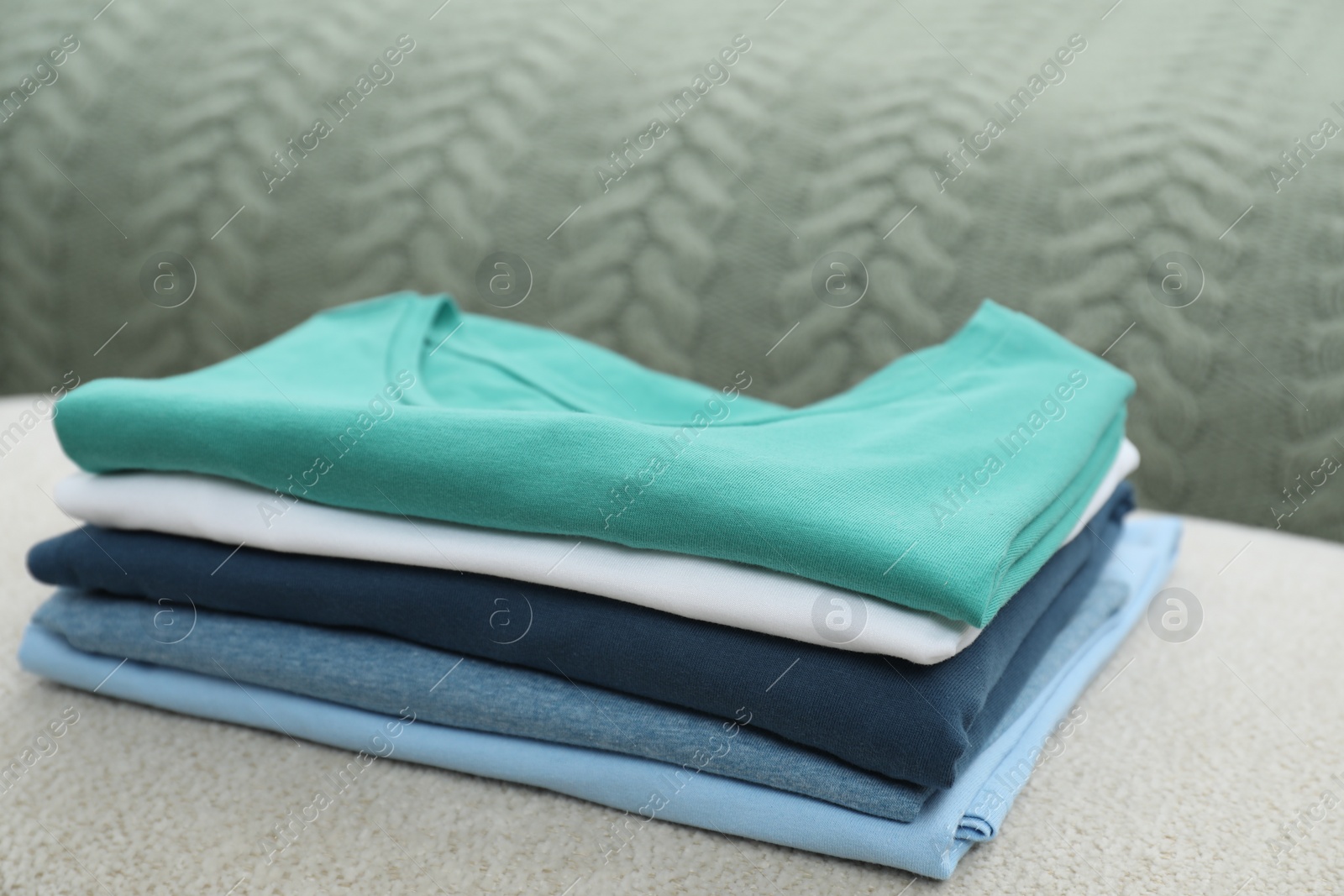 Photo of Sorting and organizing. Stack of different folded clothes on ottoman indoors