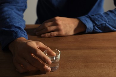 Photo of Addicted man with glass of alcoholic drink at wooden table, closeup