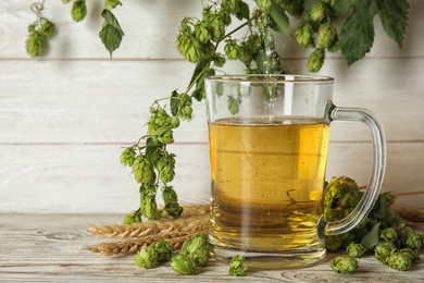 Photo of Composition with tasty beer, wheat spikes and fresh green hops on wooden table. Space for text