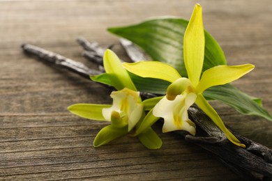 Photo of Vanilla pods, beautiful flowers and green leaves on wooden table, closeup