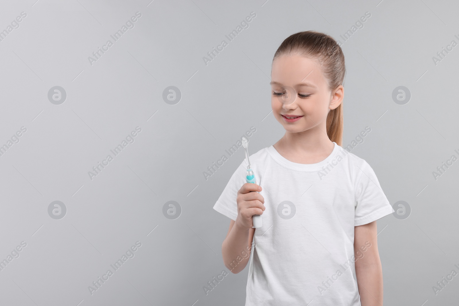 Photo of Happy girl holding electric toothbrush on light grey background. Space for text