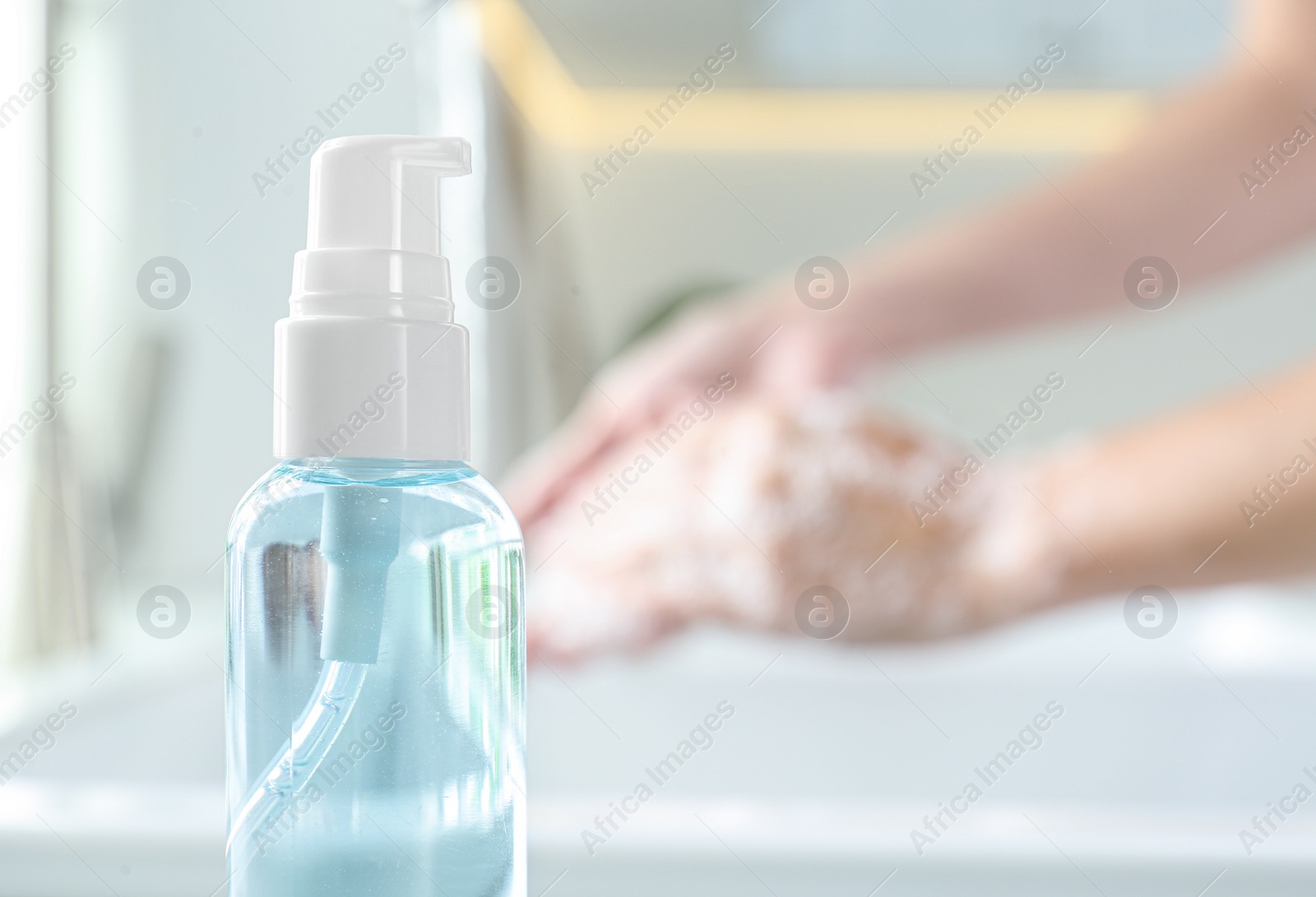 Photo of Bottle of antibacterial soap and blurred woman washing hands on background. Personal hygiene during COVID-19 pandemic