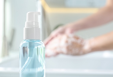 Photo of Bottle of antibacterial soap and blurred woman washing hands on background. Personal hygiene during COVID-19 pandemic