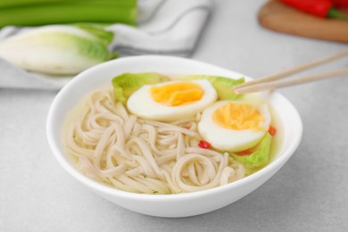 Photo of Bowl of delicious rice noodle soup with celery and egg on light grey table, closeup