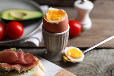 Photo of Delicious breakfast with soft boiled egg and sandwich served on wooden table