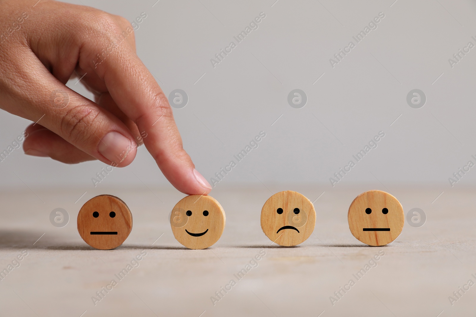 Photo of Choice concept. Woman choosing wooden circle with happy emoticon among others at light table, closeup