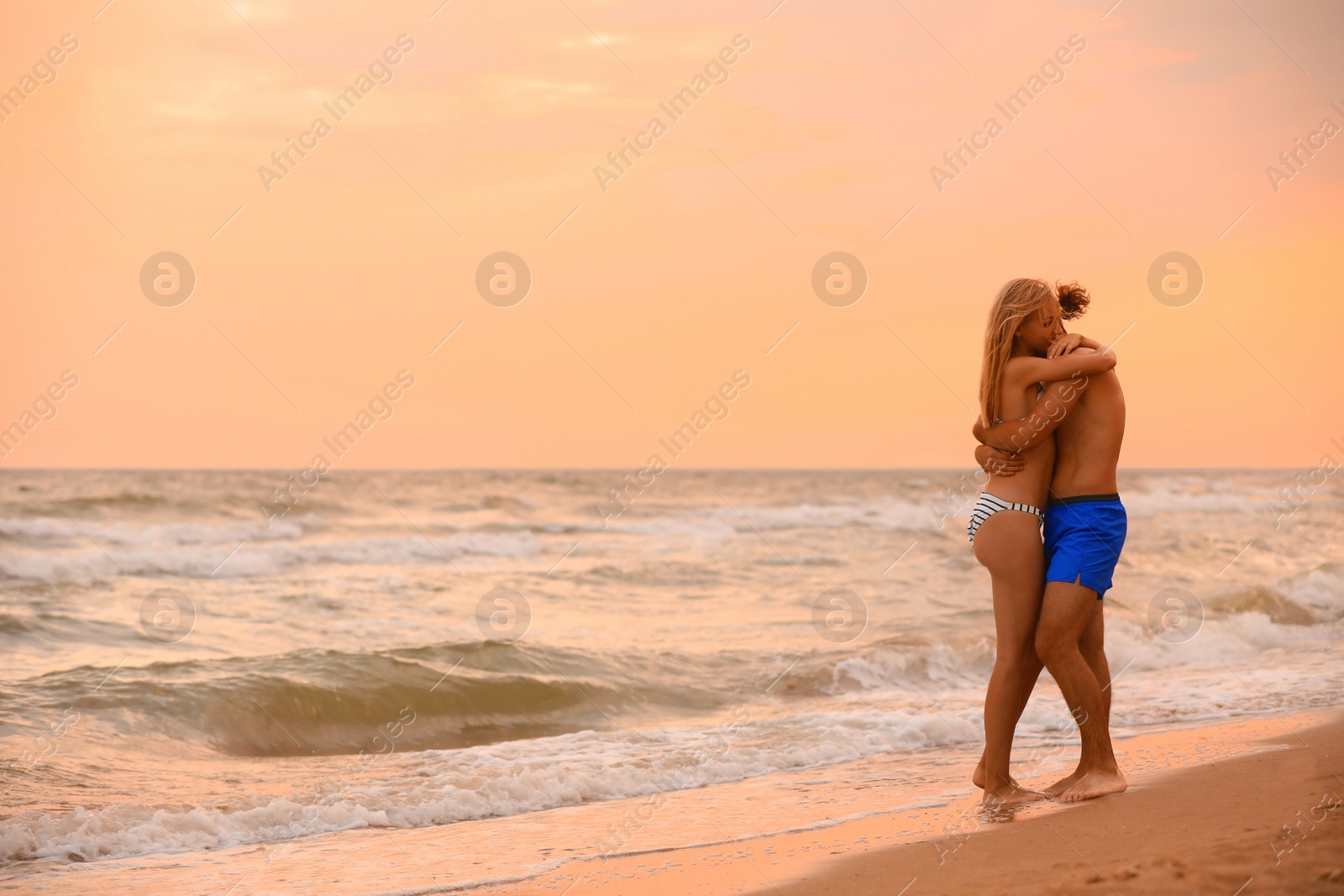 Photo of Young woman in bikini and her boyfriend on beach at sunset. Lovely couple