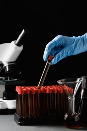 Photo of Scientist taking test tube with brown liquid from stand at grey table against black background, closeup