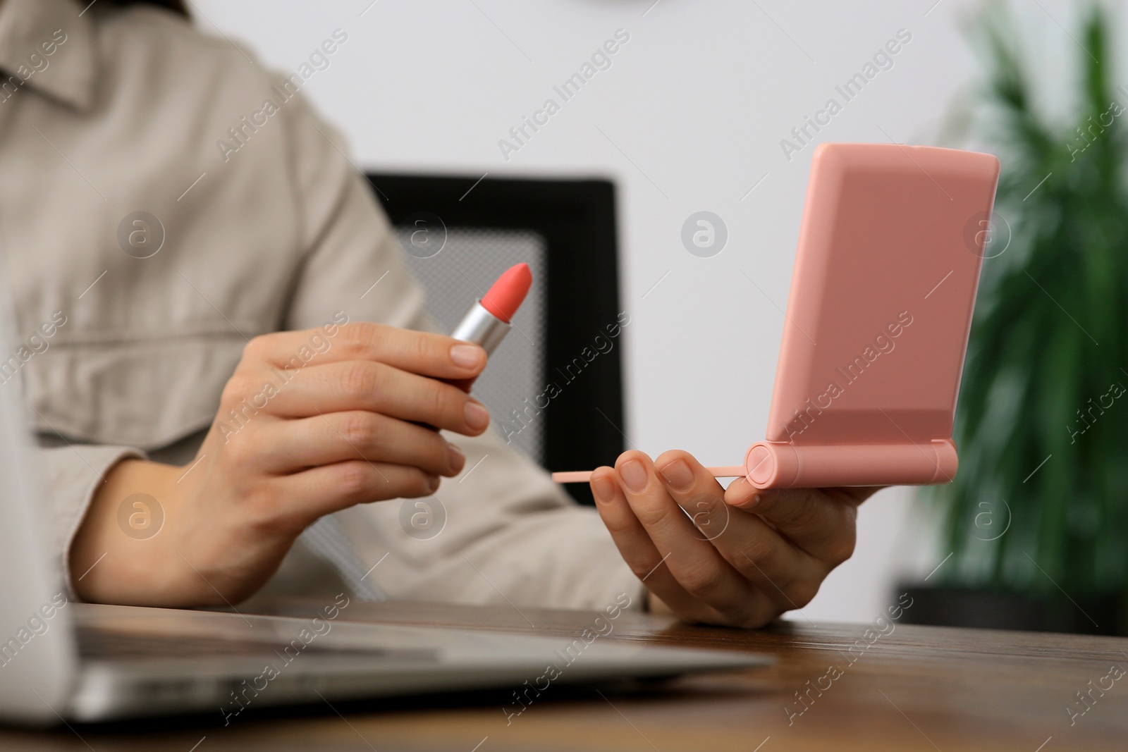 Photo of Woman with cosmetic pocket mirror and lipstick at wooden table indoors, closeup