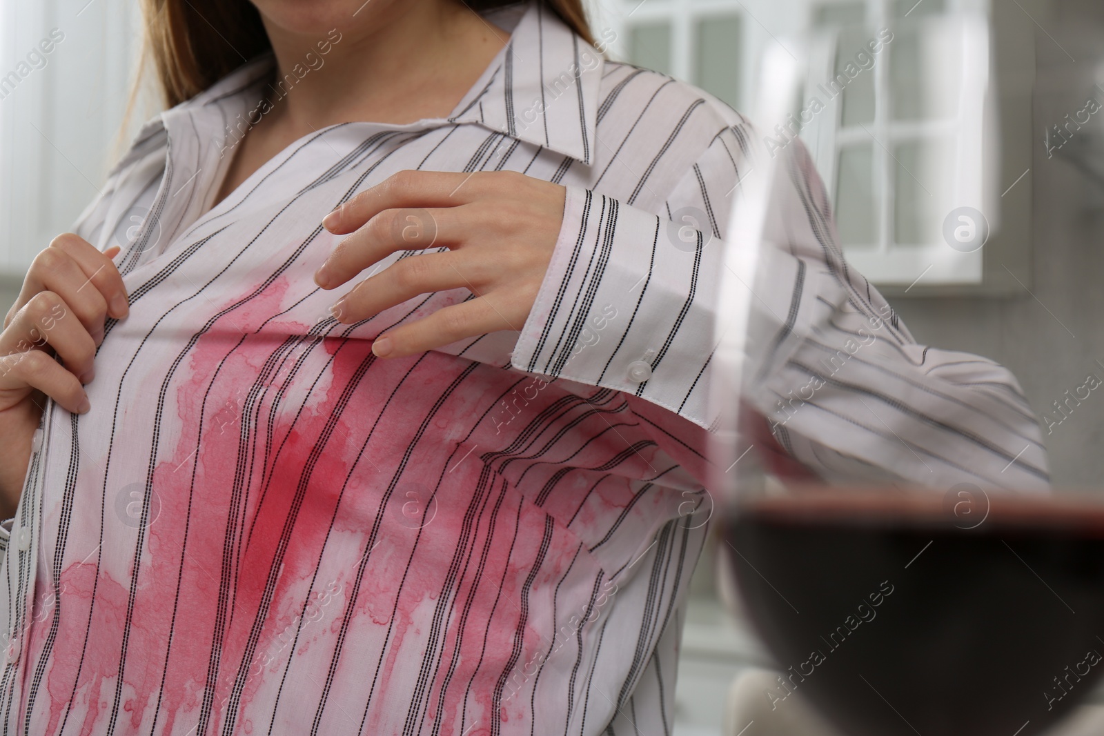 Photo of Woman with spilled wine over her shirt near glass indoors, closeup