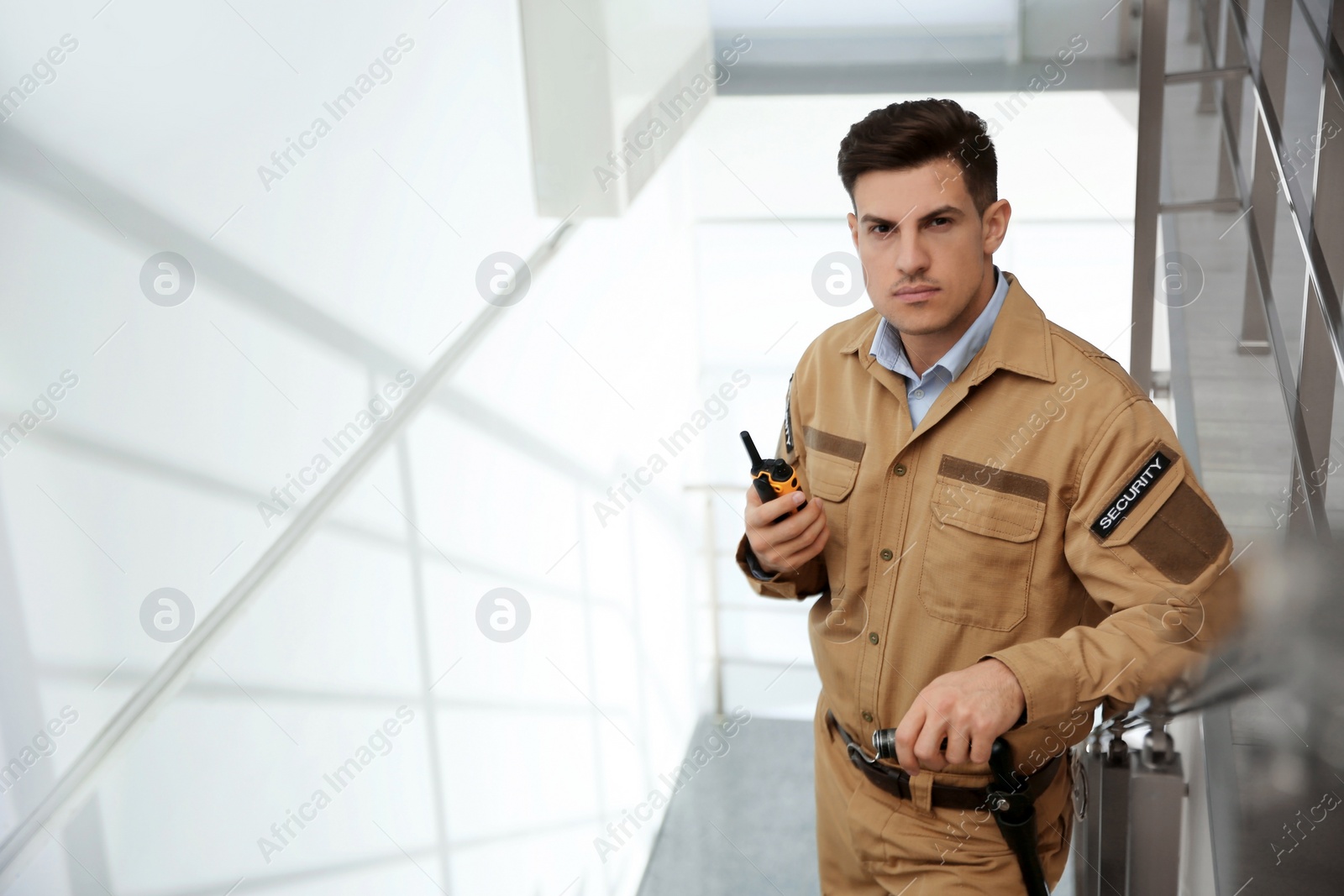 Photo of Professional security guard with portable radio set on stairs. Space for text